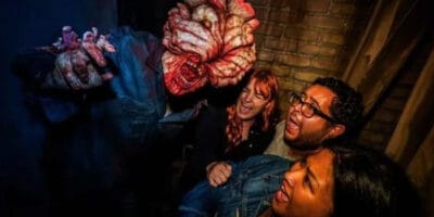 Terrified thrill-seekers react as a ghastly figure with grotesque hands looms over them in a Halloween Horror Nights haunted house attraction.