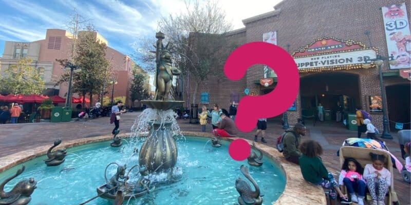 A bustling theme park scene with a detailed fountain showcasing various statues of Muppet characters. People are gathered around the Muppet-themed fountain and sitting on benches. To the right, there's an entrance to "Muppet*Vision 3D" adorned with colorful signs and decorations.