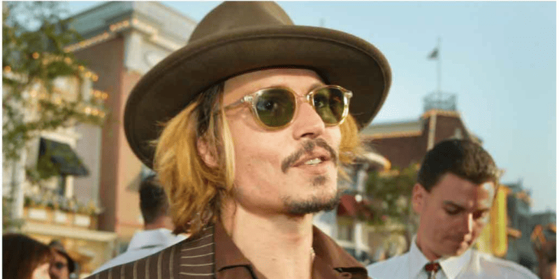 Johnny Depp at a Pirates of the Caribbean event wearing a brown jacket and inner shirt, brown hat, and sunglasses
