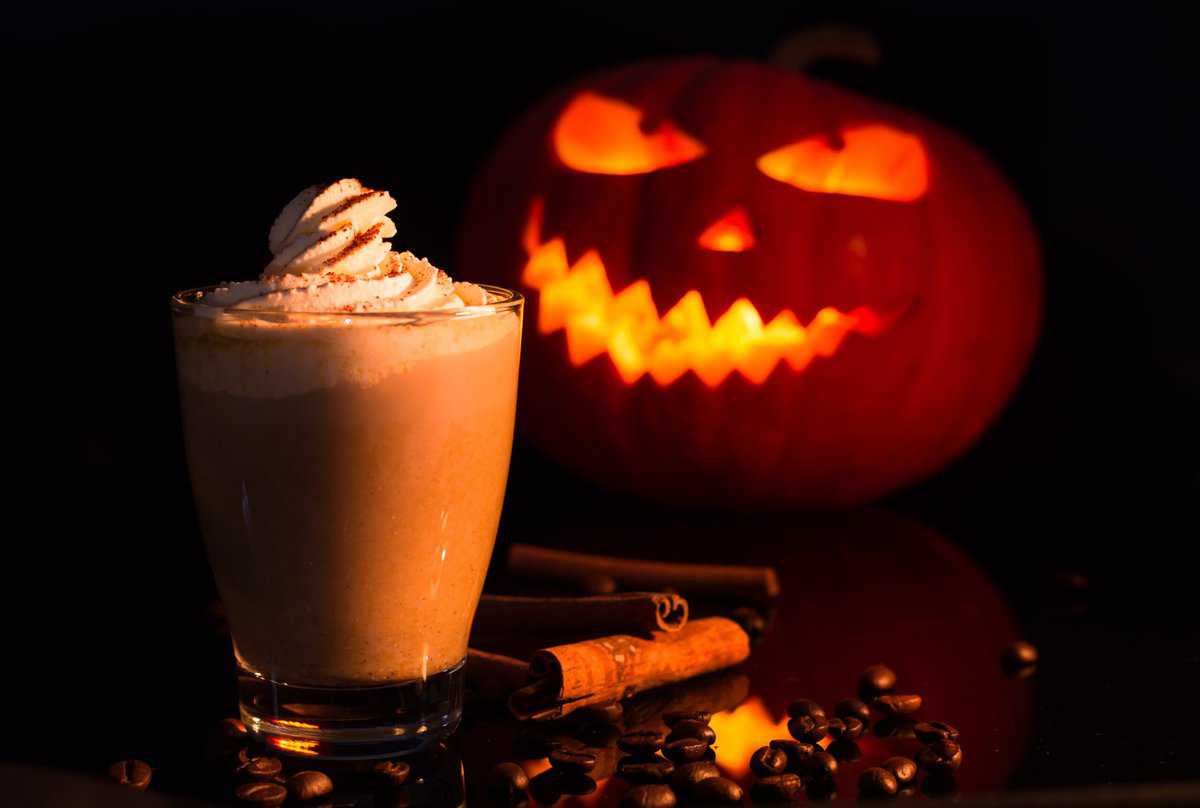 Pumpkin Spice Latte beverage topped with whipped cream and positioned in front of a carved Halloween-pumpkin