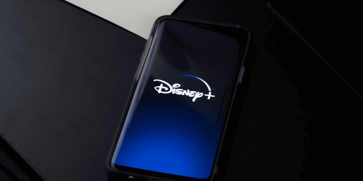 Disney plus on iPhone screen resting on black desk while charging