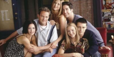 The cast of Friends huddled together, smiling at the camera