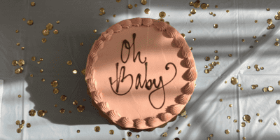 Pink 'Oh Baby' baby shower cake rested on a table and surrounded by gold sparkles