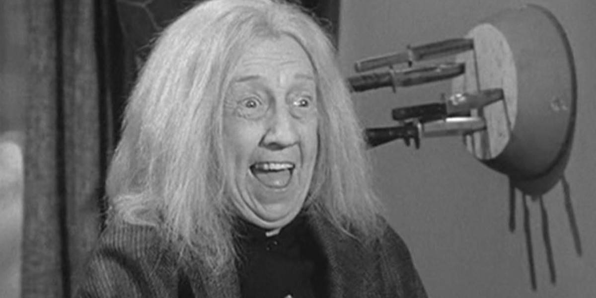 Grandma Addams (Blossom Rock) laughing in front of a wall of knives in The Addams Family sitcom