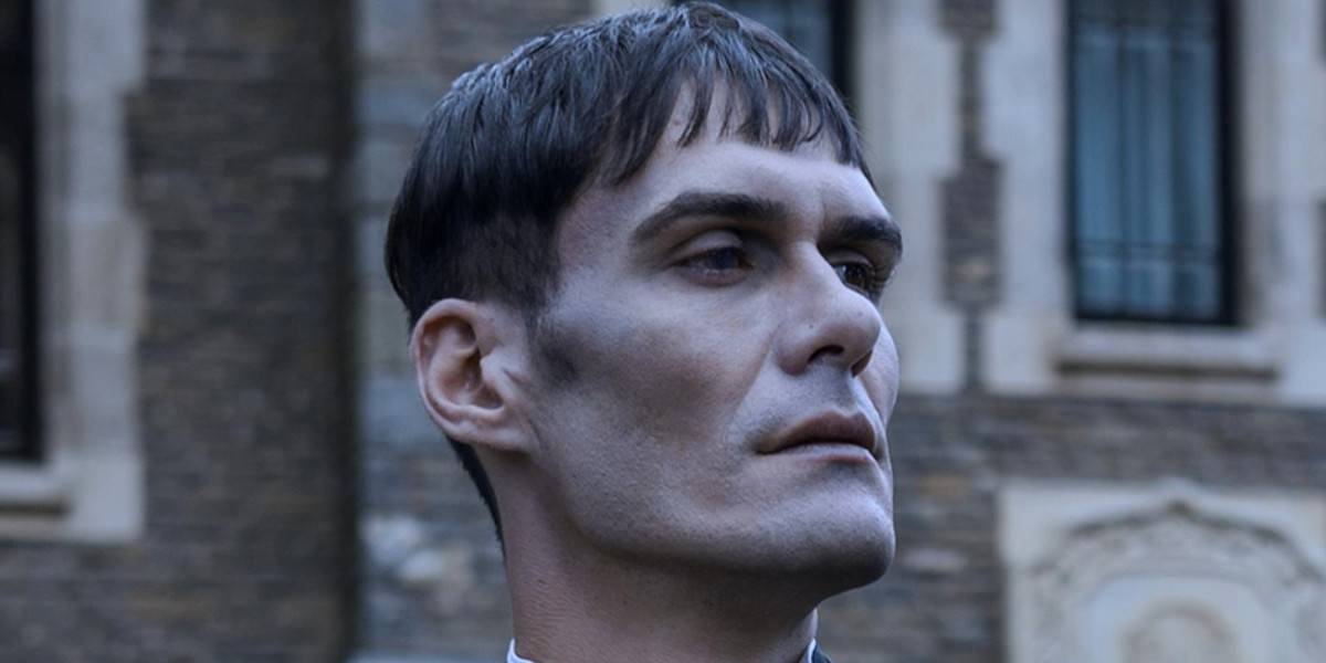 Lurch (George Burcea) standing in front of a stone building in Wednesday