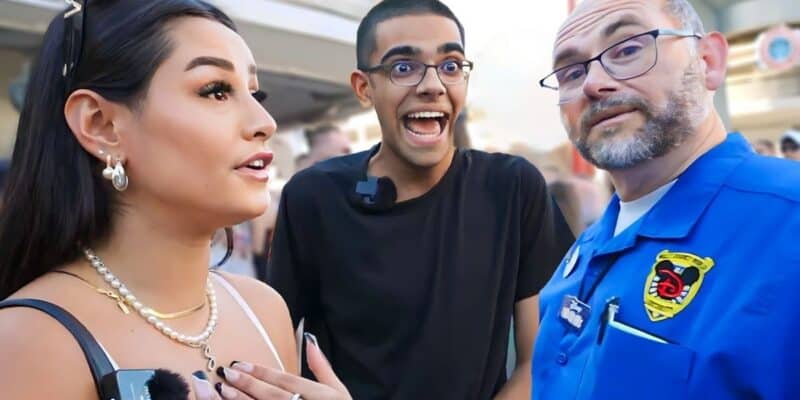 Three people are captured in conversation outdoors. A woman on the left is speaking with a man in a blue uniform on the right. Another man in the center, wearing a black shirt, is reacting with an excited expression. Despite live streaming being banned, the scene suggests a lively and engaging interaction.