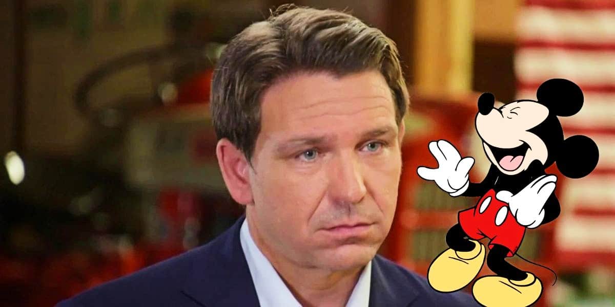 Ron DeSantis looking sad with Mickey Mouse laughing on his shoulder
