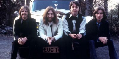 The Beatles sitting on a car for a photo