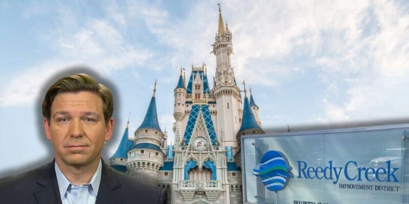 Florida Governor Ron DeSantis looking shocked with the entrance sign to the former Reedy Creek to the right and the Cinderella Castle in the background inside of Magic Kingdom at Disney World.