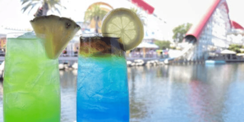 A green and a blue drink, both garnished with fruit, on a table at Lamplight Lounge in Disney California Adventure Park.