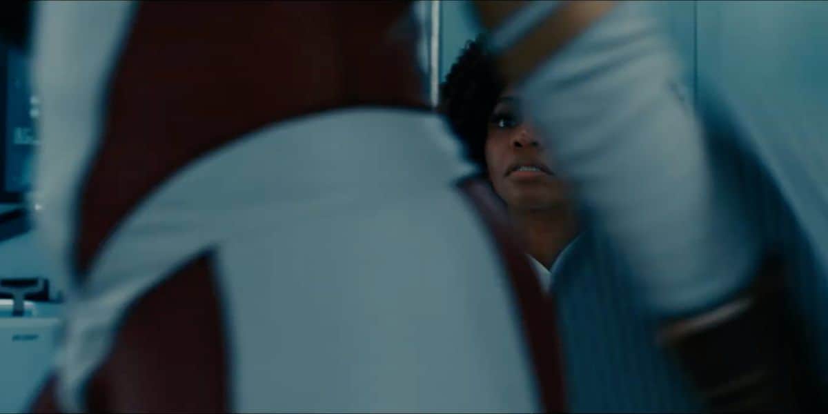 Monica Rambeau looks on in the background (partially obscured) at someone walking by in the foreground in what looks like the Binary suit, in The Marvels (2023)
