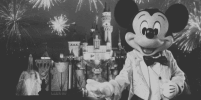 Mickey Mouse in front of Sleeping Beauty castle at Disneyland; the image has been turned to black & white to convey some secrets are being hidden.