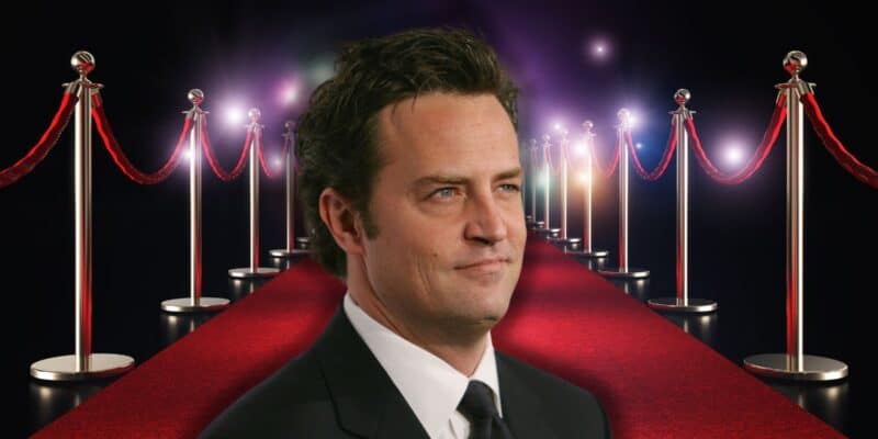 Matthew Perry on the red carpet with paparazzi camera flashes in the background.