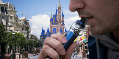 A man smokes a vape in front of Cinderella Castle on Main Street, U.S.A.