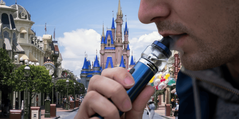 A man smokes a vape in front of Cinderella Castle on Main Street, U.S.A.