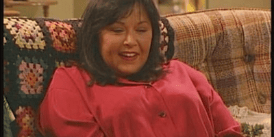 Roseanne laughs on the Conner family's couch.