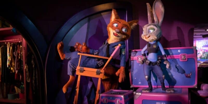 Two character figures resembling a fox and a rabbit, dressed as police officers, are displayed with themed props and luggage in a dimly lit, colorful setting at Shanghai Disneyland.
