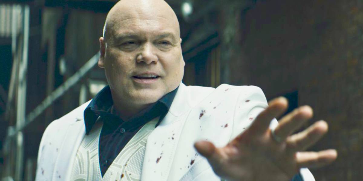 Vincent D'Onofrio in a white suit with blood splatter on it reaching out with a hand and smiling