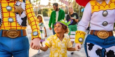 A child wearing Little Green Men Mickey ears holding hands with Woody and Jesse