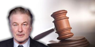 Alec Baldwin inside of a courtroom awaiting trial with a gavel to his right.
