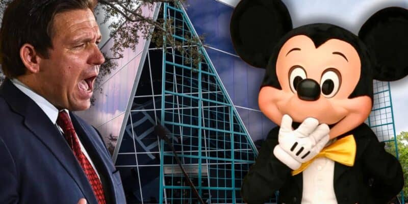 Florida Governor Ron DeSantis speaks on a podium in front of the CFTOD building with Mickey Mouse with his hands over his mouth.
