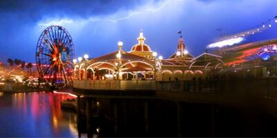 A striking image of Disneyland at night featuring a lit-up carousel and Ferris wheel, with a dramatic lightning bolt illuminating the sky in the background.