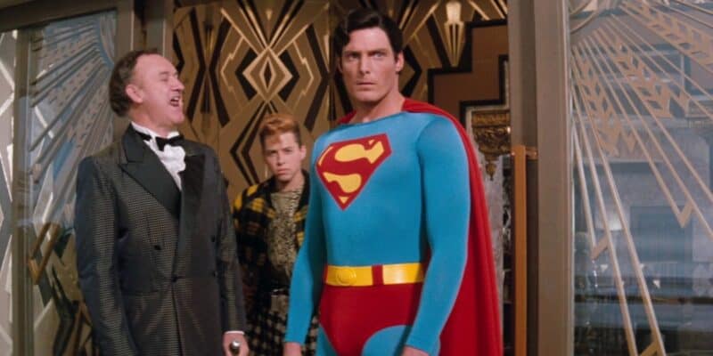 Superman (Christopher Reeve) looking upset as Lex Luthor (Gene Hackman) laughs and Lenny Luthor (Jon Cryer) hides in the background