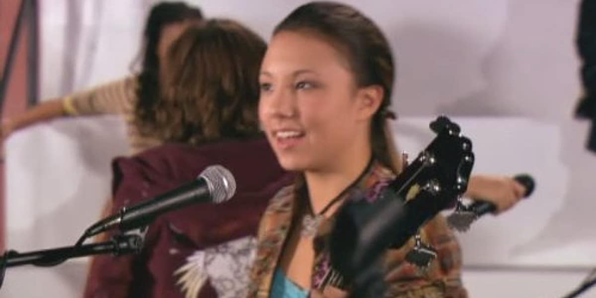 Allie DiMeco standing at a microphone with a guitar.
