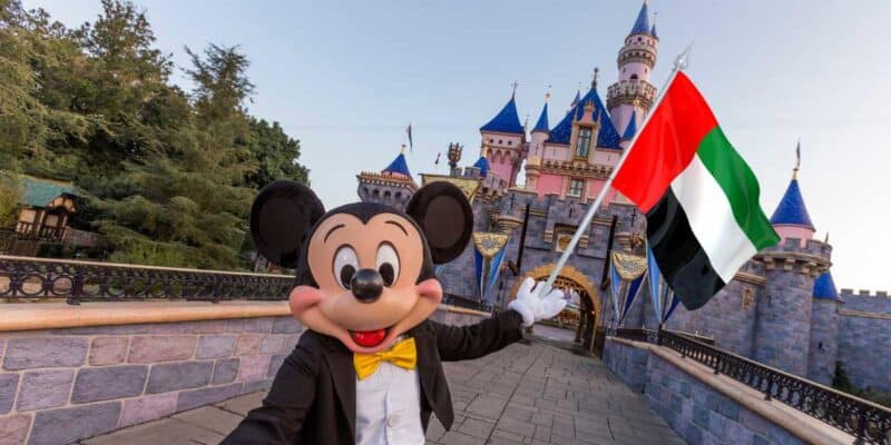 Mickey Mouse holding a United Arab Emirates flag in front of Sleeping Beauty Castle