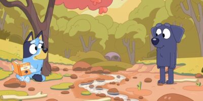 Two cartoon dogs, one named Bluey with a book and the other darker blue, stand in a muddy forest with trees and rocks in the background.