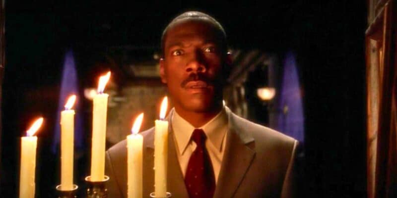 A man in a suit appears surprised or intrigued, standing in a dimly lit room lit by multiple candles with tall flames.