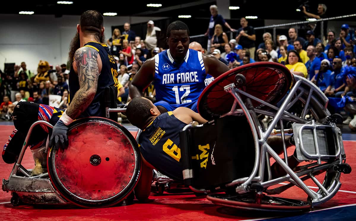 Two wheelchair basketball players collide during a game, with one player from the navy team on the ground trying to retrieve the ball, as a player from the air force watches. fans in the background spectate eagerly at the Department of Defense Warrior Games, which will take place at Disney World in two months.