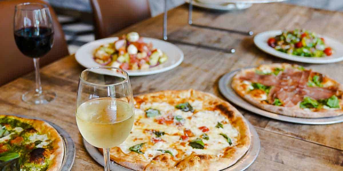 A cozy dining table with a variety of pizzas and salads, accompanied by glasses of red and white wine.