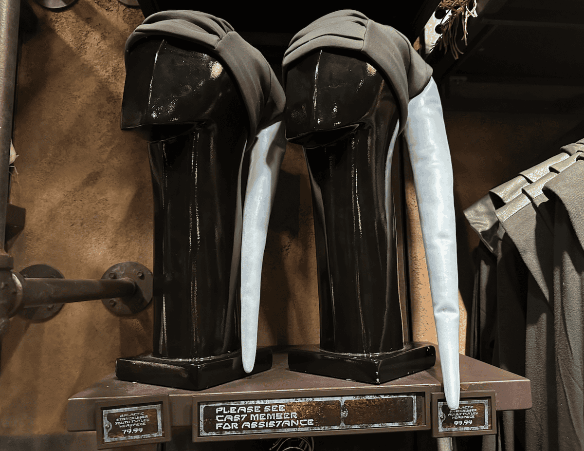 A pair of glossy black boots with silver knee guards displayed on a stand, possibly themed merchandise from a fantasy or science fiction franchise, with price tags indicating $79.99 for the boots and $49.99 for the kneepads.