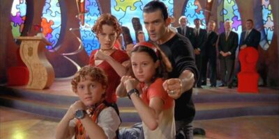 A still from 'spy kids' featuring two kids in spy gear with their parents behind them in a colorful, puzzle-themed room, all posed ready for action.
