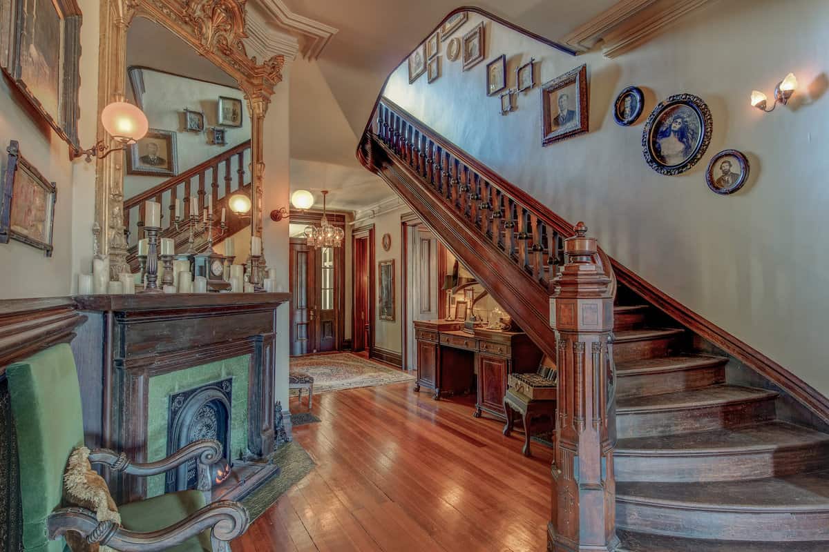 Elegant vintage interior with a wooden staircase, ornate banisters, hardwood floors, and antique decorations evoking a sense of historical charm.