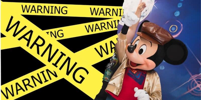 Mickey Mouse with his hands raised up with a warning sign to the left, inside of the Disney D23 Fan Expo.