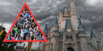 Crowds of visitors gather in front of a fairytale castle under a dramatic cloudy sky, with a red triangle superimposed over the image.
