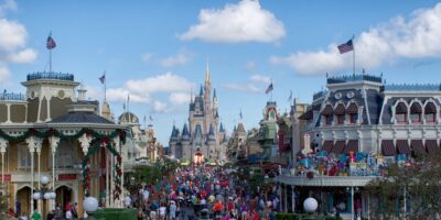 A bustling main street filled with visitors leading up to a fairy tale castle under a blue sky, capturing the magic of a famous theme park.
