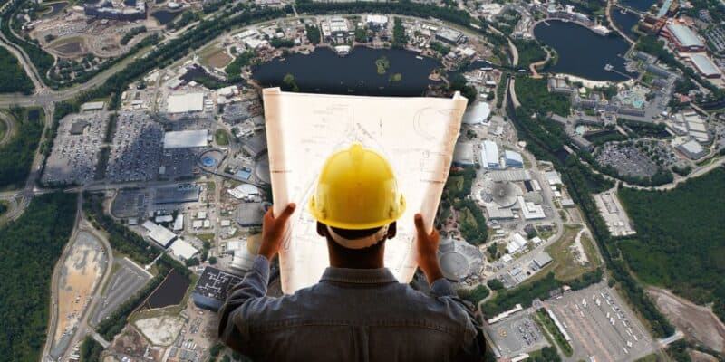 An aerial view of a cityscape with a Disney Imagineer holding blueprints, wearing a hard hat, suggesting they are planning or overseeing construction or development at Disney World.
