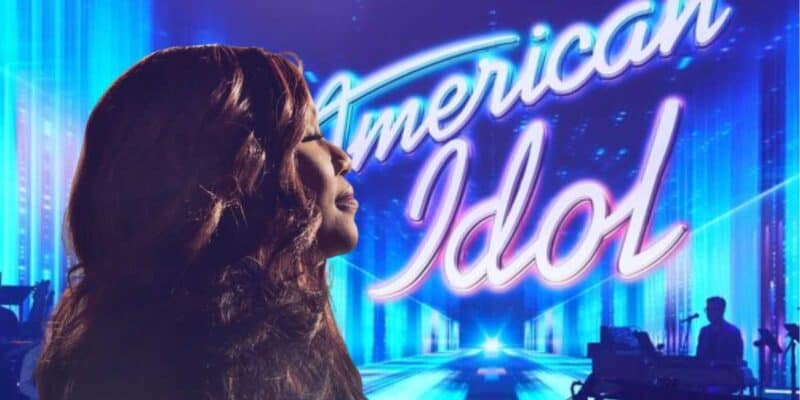 A silhouette of a woman, Mandisa, singing passionately, her head tilted back, with a brightly lit "american idol" sign and stage in the background, suggesting a musical performance.
