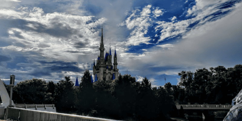 A captivating view of a fairytale castle with spires, under a dramatic sky with scattered clouds and beams of sunlight, surrounded by lush greenery.
