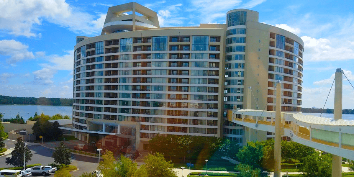 Modern curved building overlooking a body of water, with a sky bridge on the side, under a partly cloudy sky.