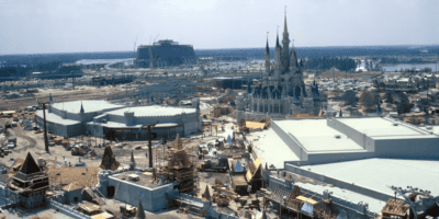 Aerial view of a large construction site with multiple buildings under construction, including a prominent fairy tale castle, amidst vast cleared land with scattered trees.