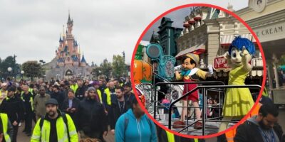 A crowd of people at disneyland with a focus on a parade float featuring animated characters pinocchio and jiminy cricket, the latter marked with a red crossed circle indicating disapproval or prohibition.
