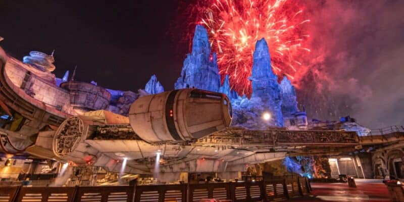 Fireworks illuminate the night sky above a parked Millennium Falcon at a 'Star Wars'-themed park attraction, casting a spectacular glow on the intricately detailed landscape.
