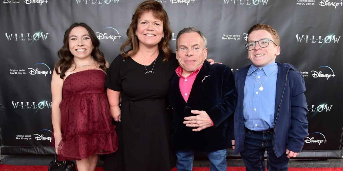 Four people smiling at the camera on a red carpet event for disney+'s "willow," with a backdrop featuring the show's logos. two men in the foreground and two women standing behind them.