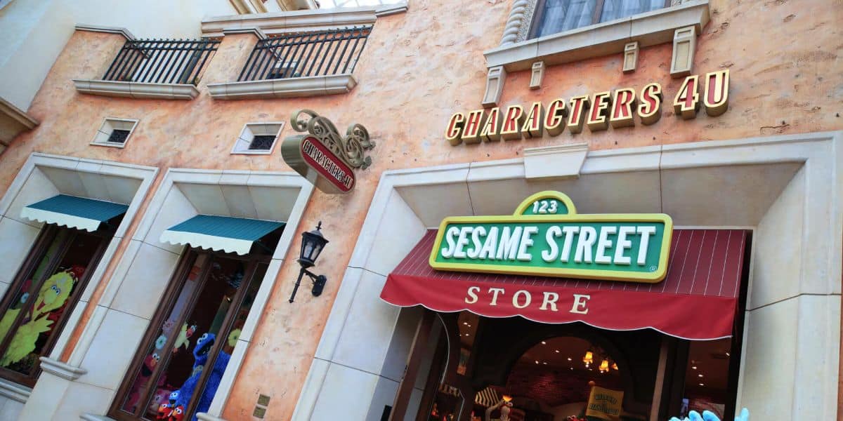 Exterior view of a Sesame Street store, featuring colorful signage and a façade resembling a city street building, with another sign that says Characters 4 U.