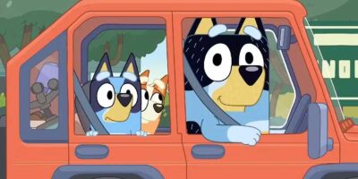 Two animated dogs, one wearing a blue shirt, are sitting in the front seats of a red van with an open window. another small dog is in the back seat looking out.