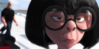 A close-up of a Pixar character with straight black hair, large round glasses, and an unimpressed expression. In the background, a muscular character in a black shirt and blue pants is walking away, slightly out of focus.